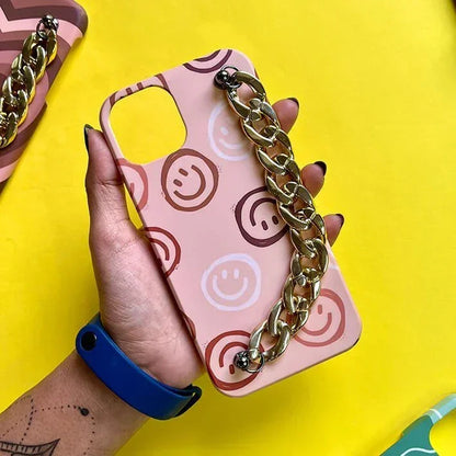 Peach phone case with smiley face pattern and gold chain handle, held in hand on yellow background.